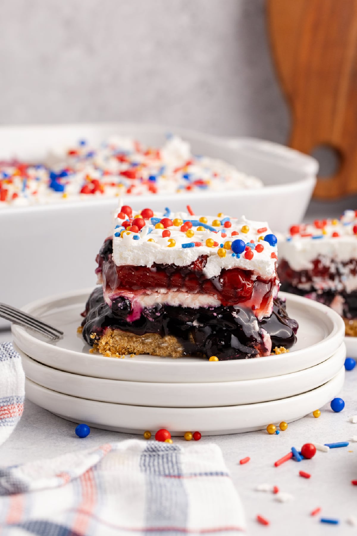 A slice of Berry Dessert on a plate with a fork with dessert behind it on a table