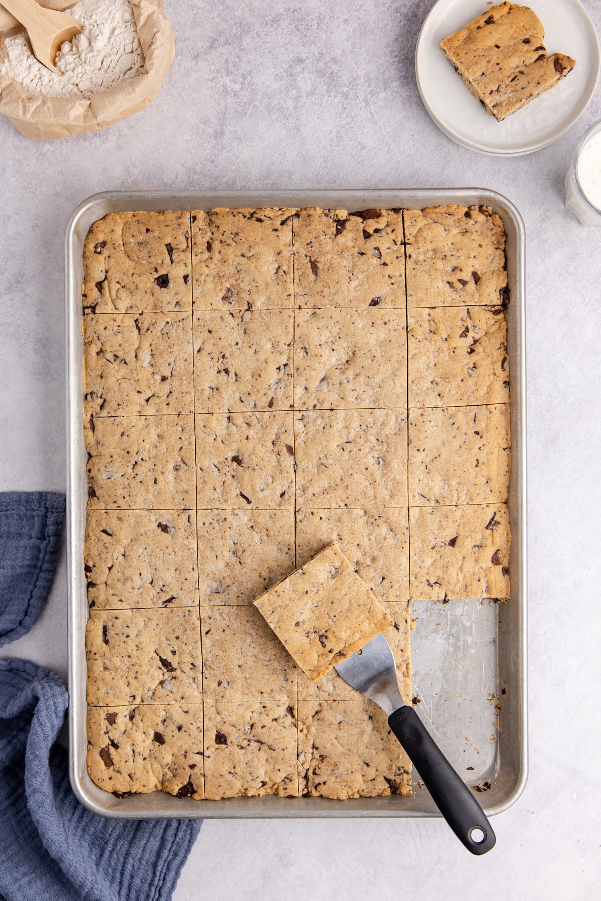 Sliced cookies in sheet pan with one square slice on spatula on top