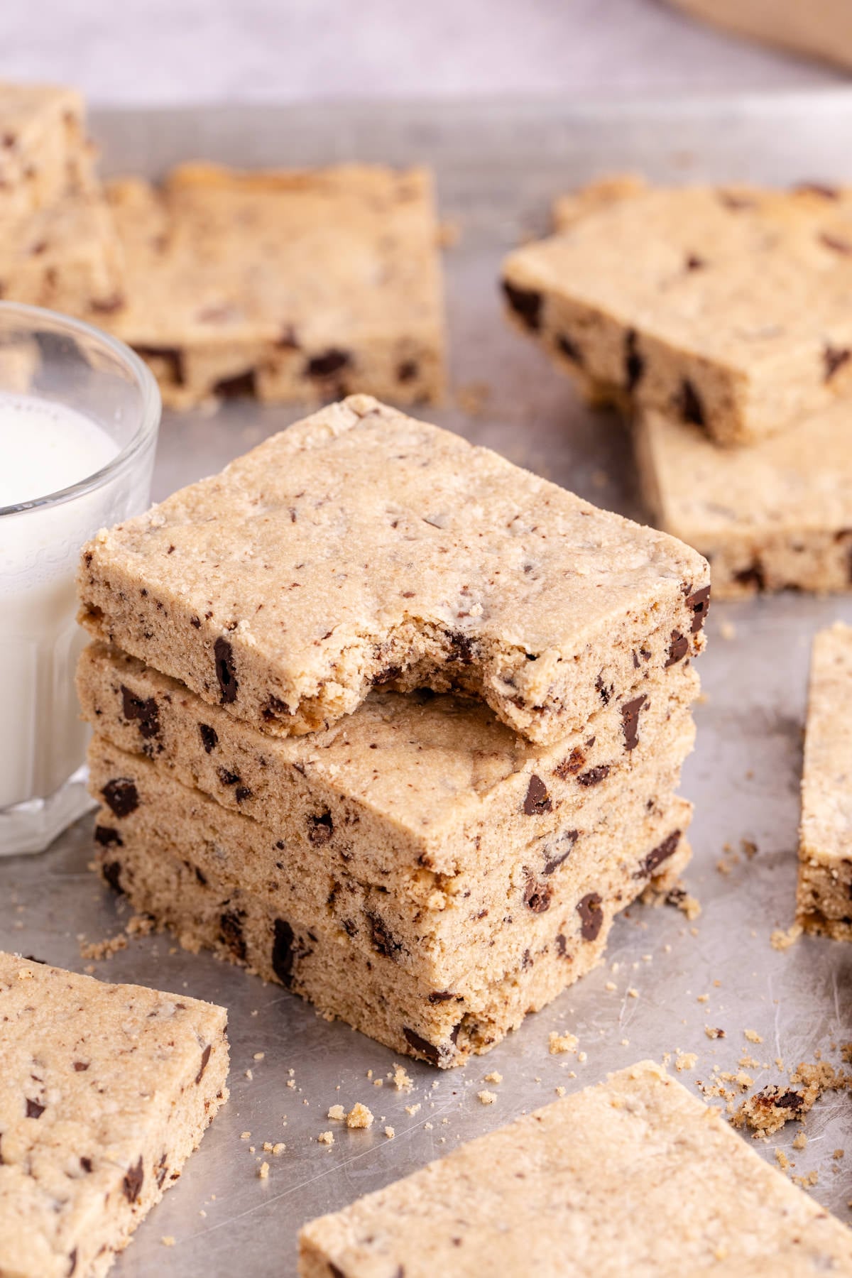 A stack of slices of Sheet Pan Cookie on pan with top slice missing a bite with other slices scattered around