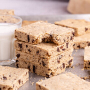 A stack of slices of Sheet Pan Chocolate Chip Cookie with top cookie missing a bite on pan with other slices scattered around