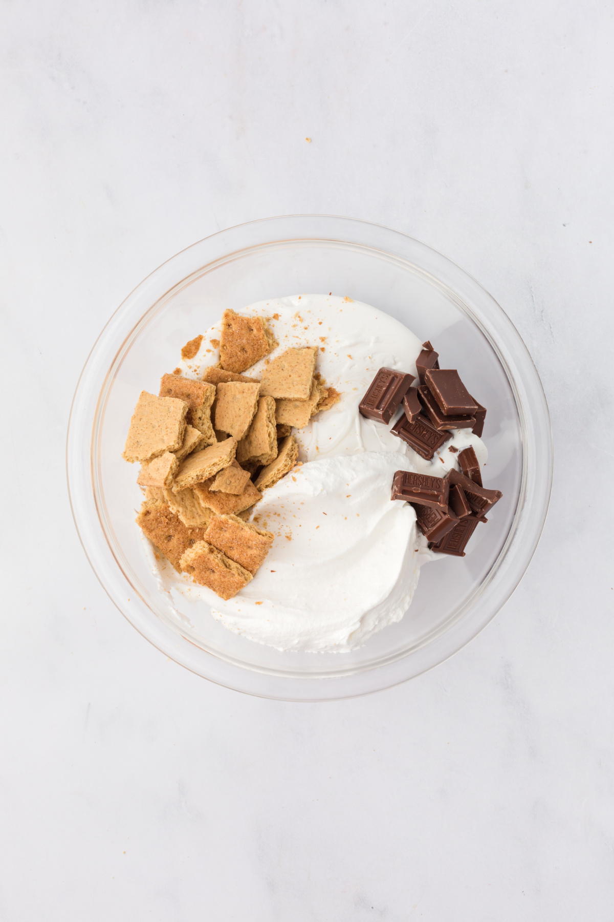 Marshmallow fluff, whipped topping, mini Hershey bars, and crumbled Graham crackers in a mixing bowl.