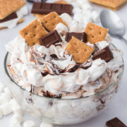 A bowl of S'mores Fluff garnished with graham cracker pieces and chopped chocolate on a table.