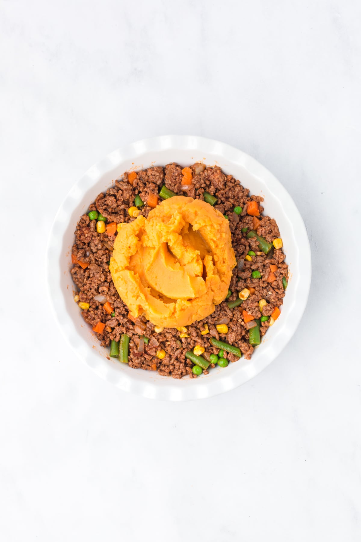 The ground beef mixture added to a prepared pan with sweet potato mash on top.