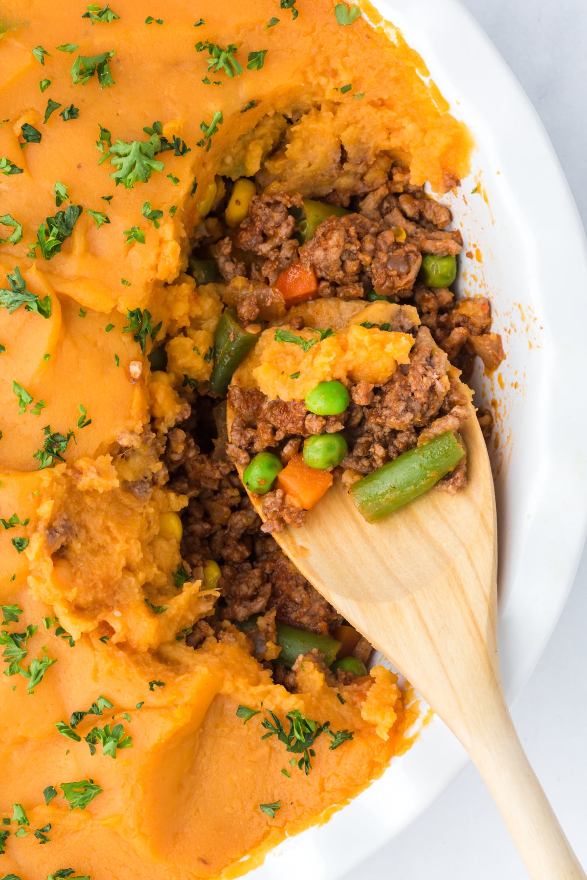 Shepherd's pie with sweet potatoes being scooped out with a wooden spoon.
