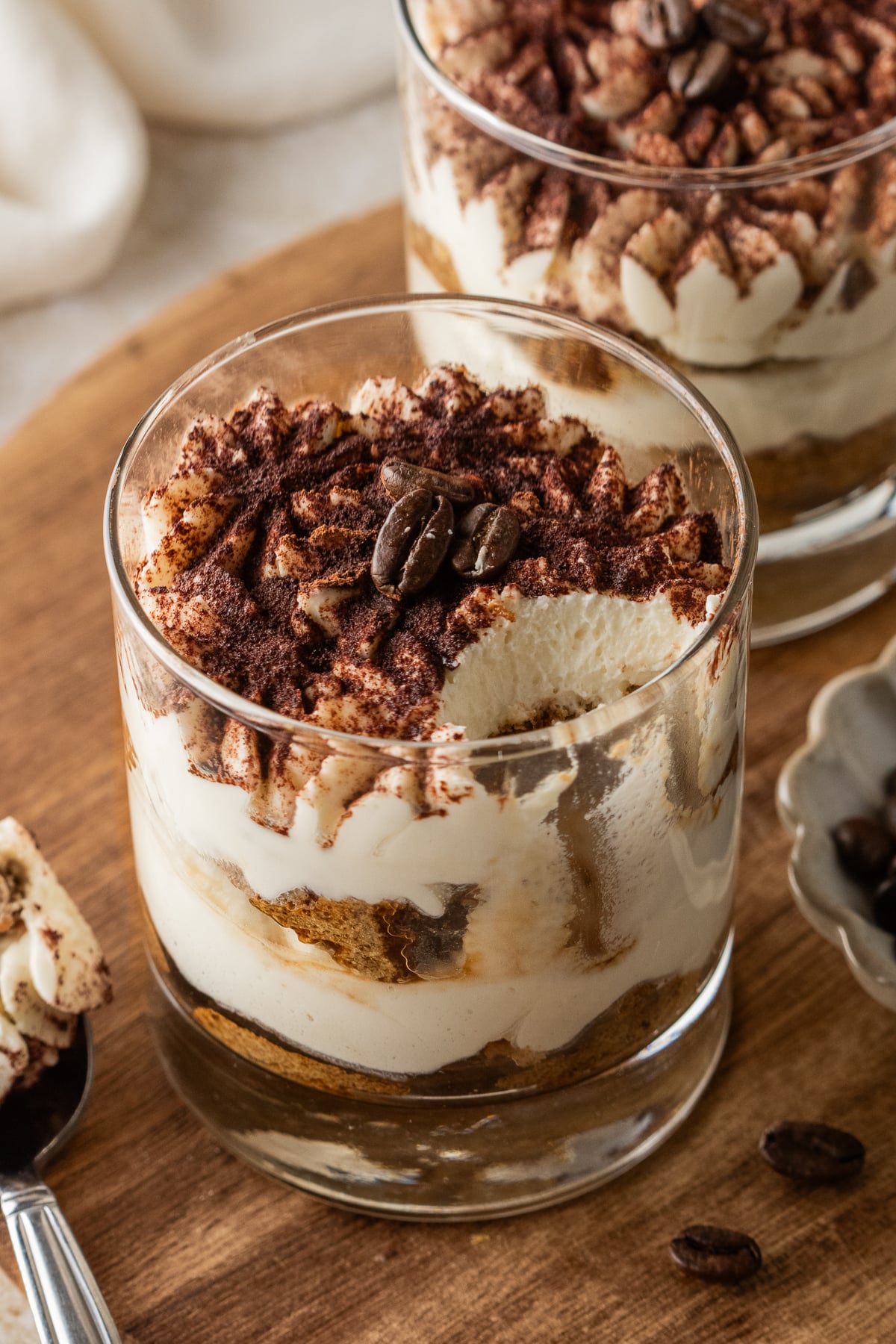 A spoon on the side with some of the tiramisu taken out of the glass.