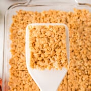 A square on a spatula held in air above pan full of butterscotch rice krispie treats