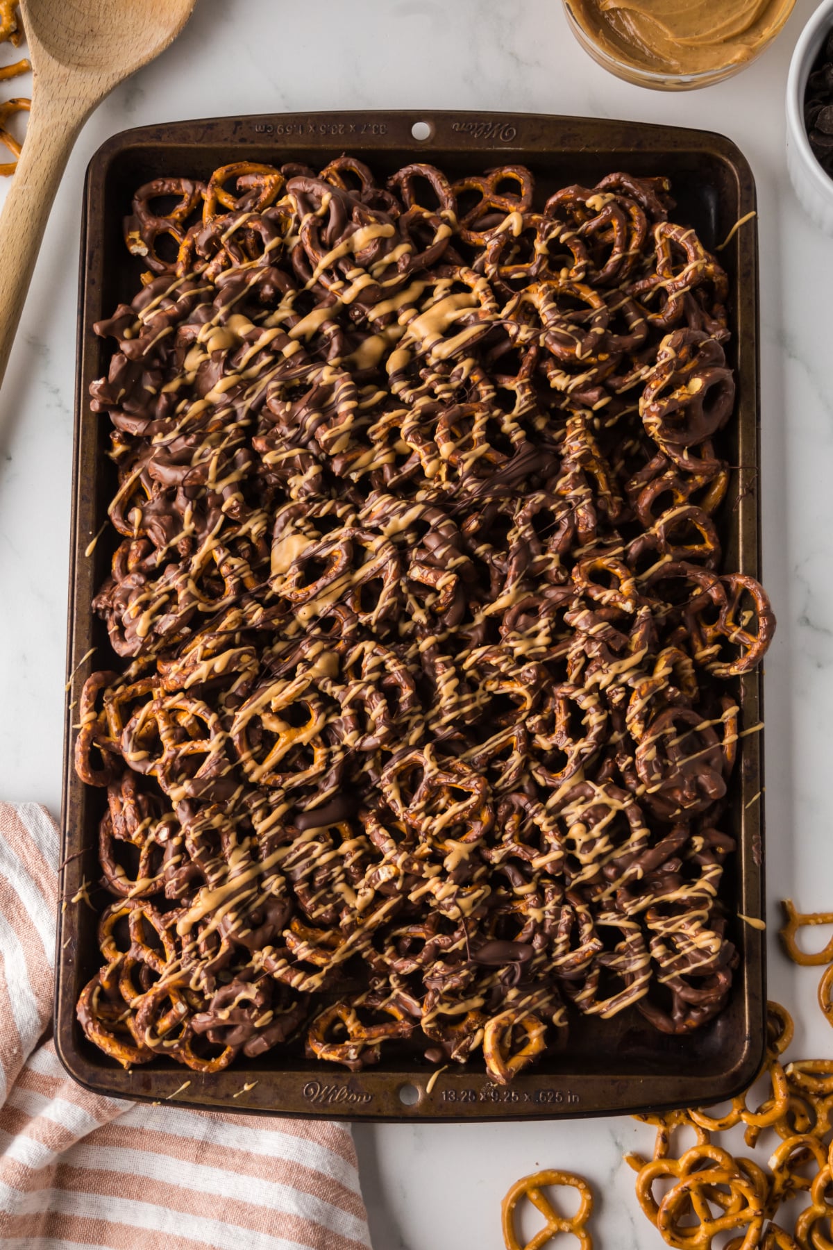 pretzels spread out on baking sheet to set after being drizzled with more peanut butter and chocolate