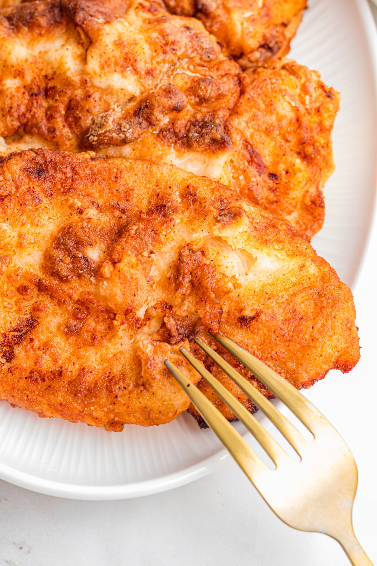 A fork poking a piece of fried chicken on a plate.