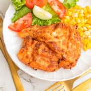 Fried chicken breast on a plate with corn and a salad.