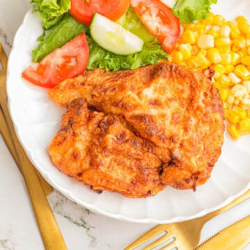 Fried chicken breast on a plate with corn and a salad.