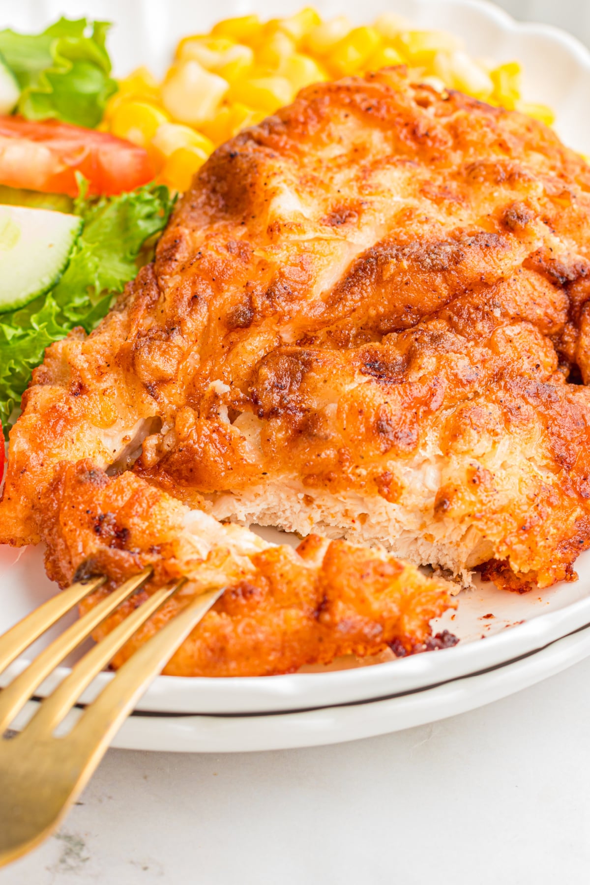 A piece of crispy chicken breast being picked up with a fork.