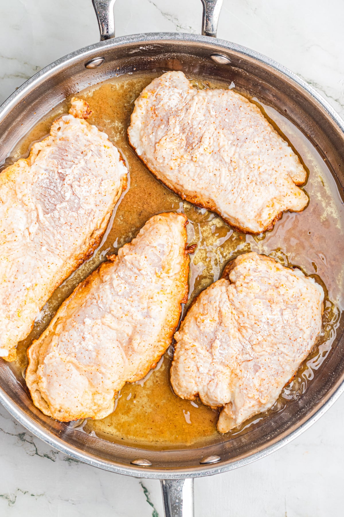 The coated chicken frying in a skillet.
