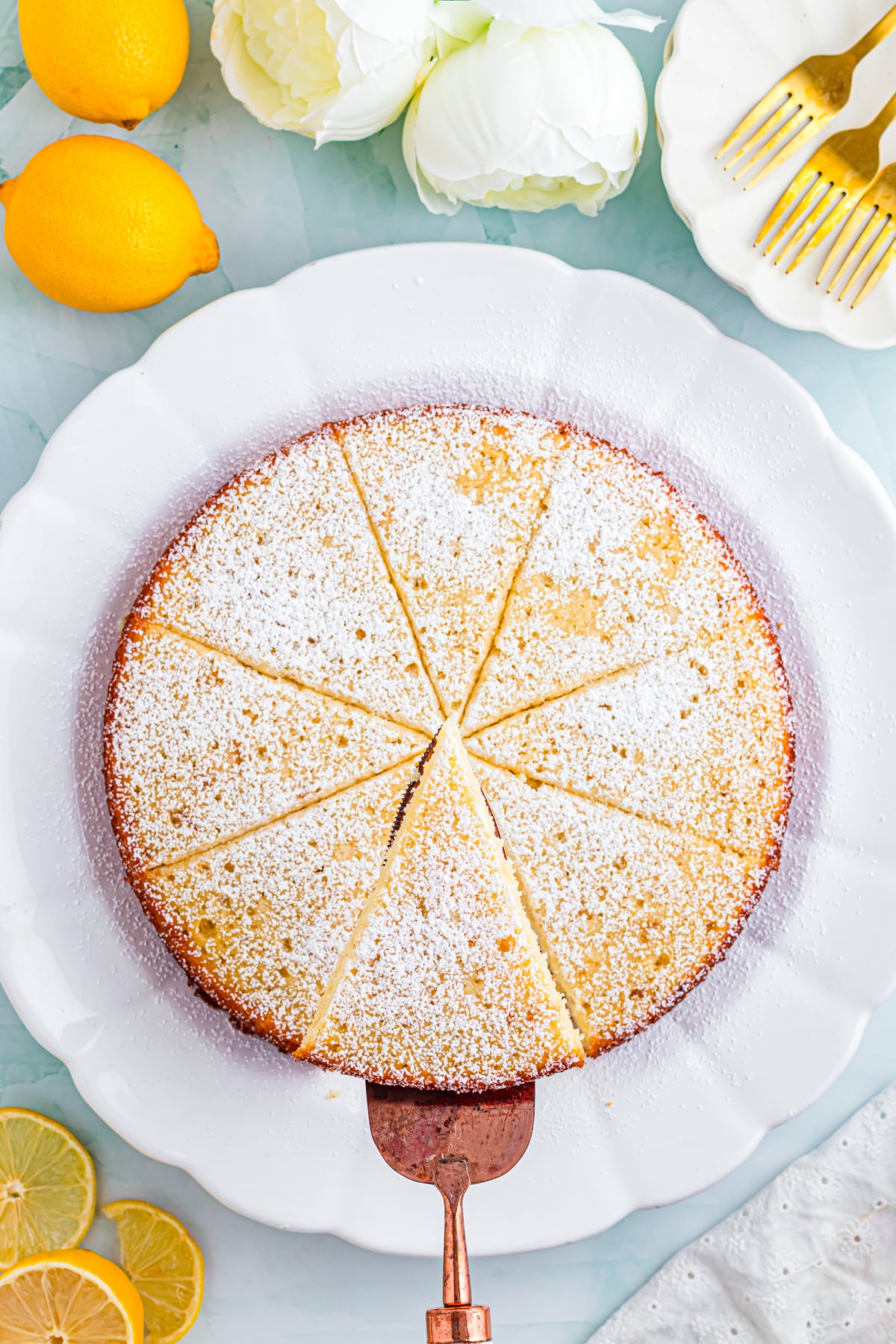 A full lemon cake with powdered sugar on top on a white plate.