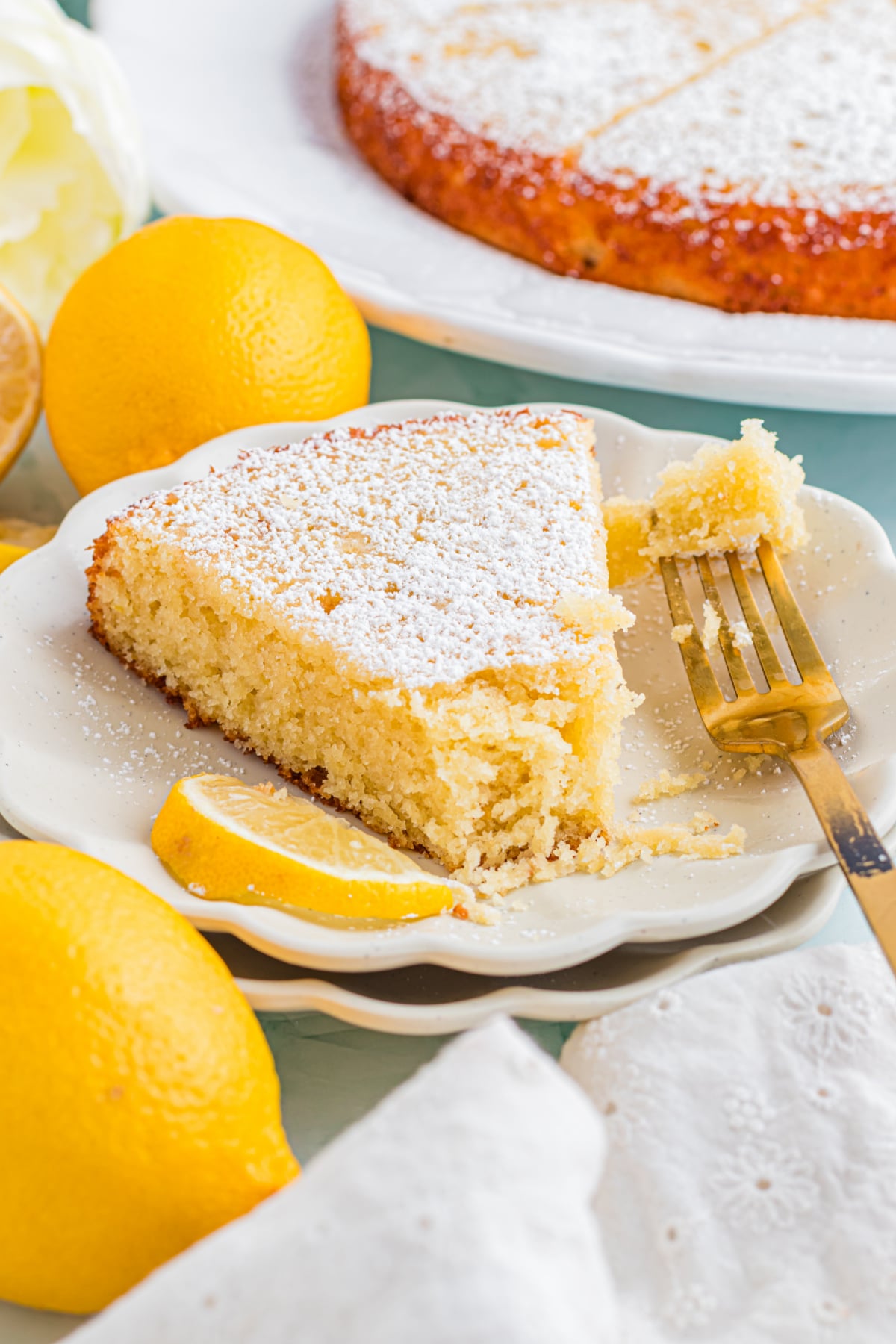 A fork with a piece of lemon cake on it resting next to a slice of cake.