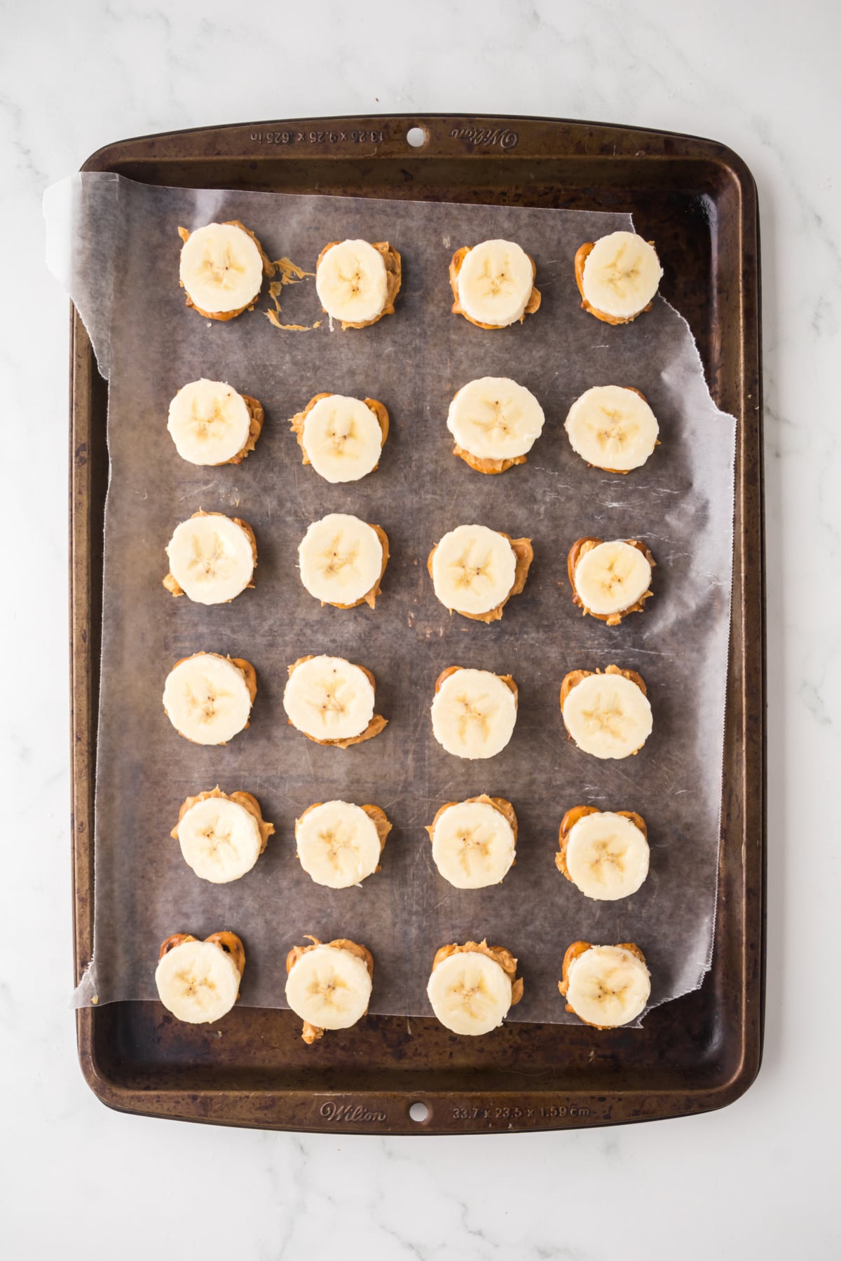 A layered pretzel covered in peanut butter and a banana on a parchment covered cookie sheet