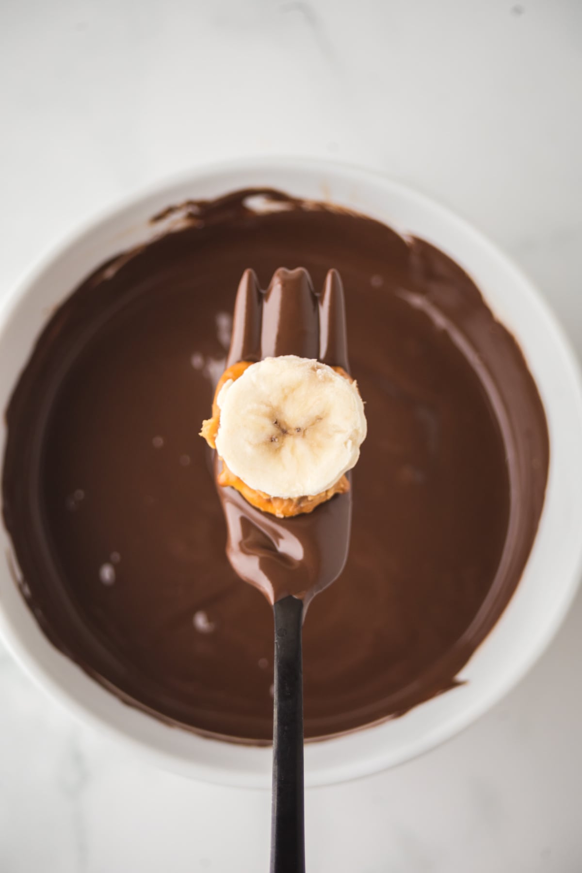 A fork holding a layered pretzel above melted chocolate ready to dip