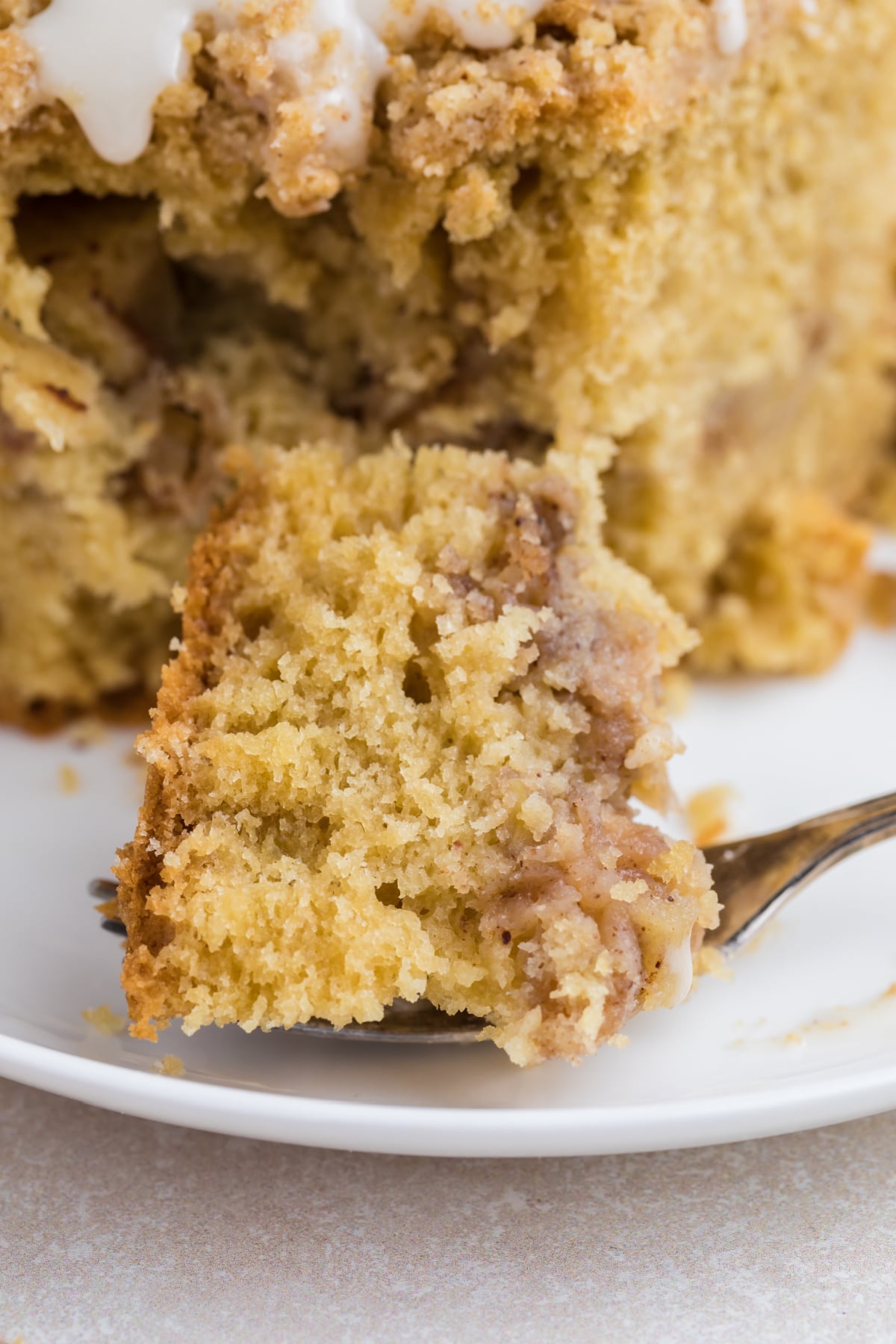 Fork holding a bite of Cake with cinnamon apples, crumb topping, and vanilla glaze on a plate.