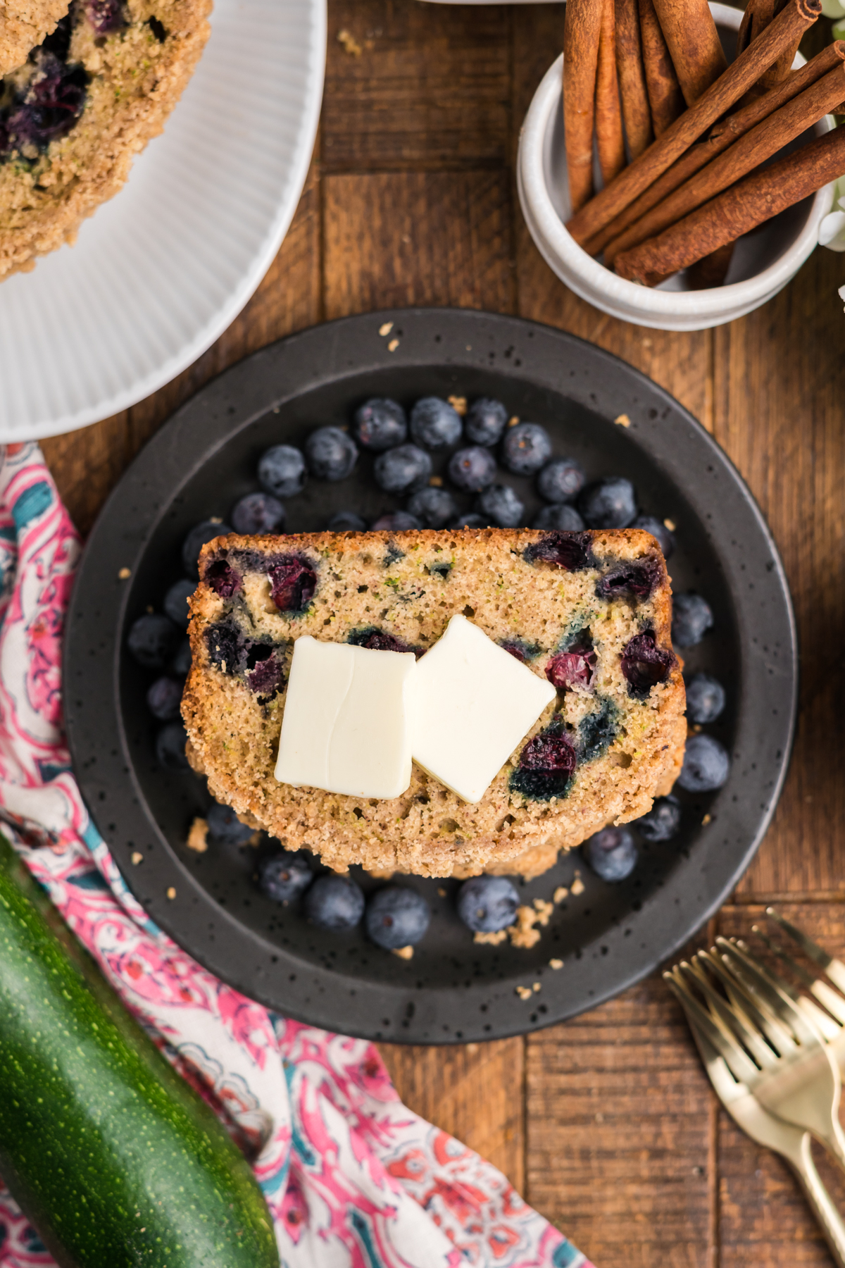 Slice of zucchini blueberry bread topped with butter and fresh blueberries on a plate.