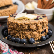 A stack of two slices of Blueberry and Zucchini Bread with butter on top on a plate.