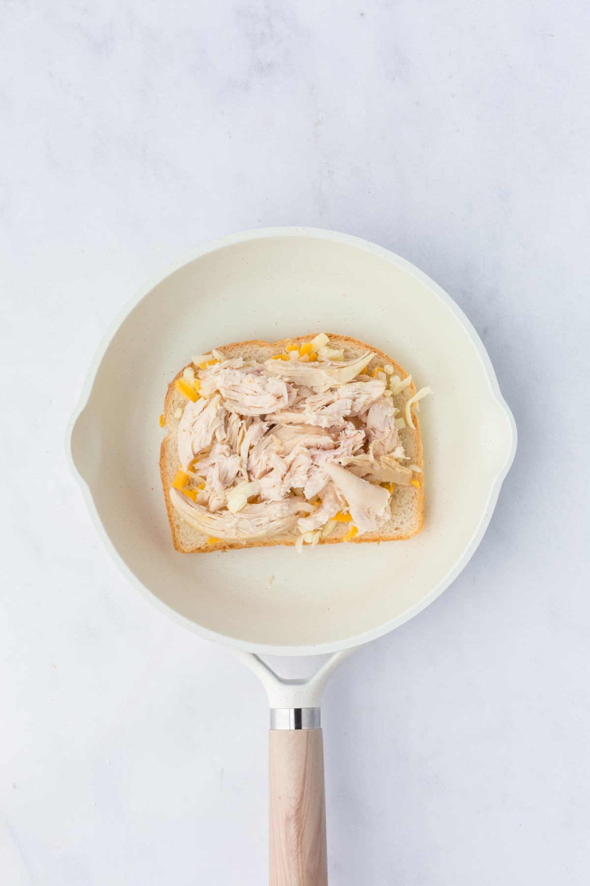 A slice of bread, butter side down, in the frying pan topped with shredded Colby Jack cheese and chicken.
