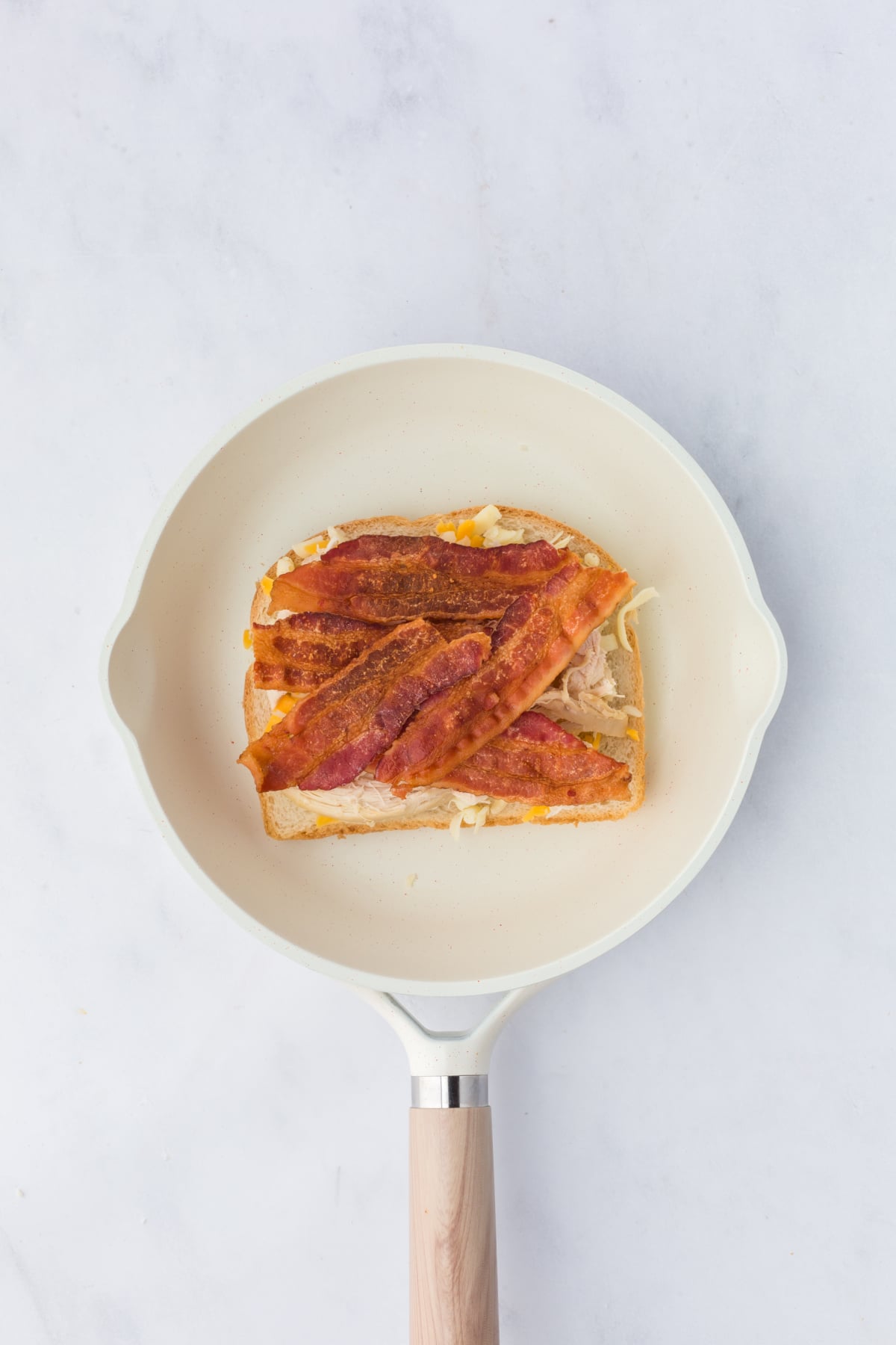 Bacon, a sprinkling of shredded cheese and remaining slice of bread, butter side up are added.