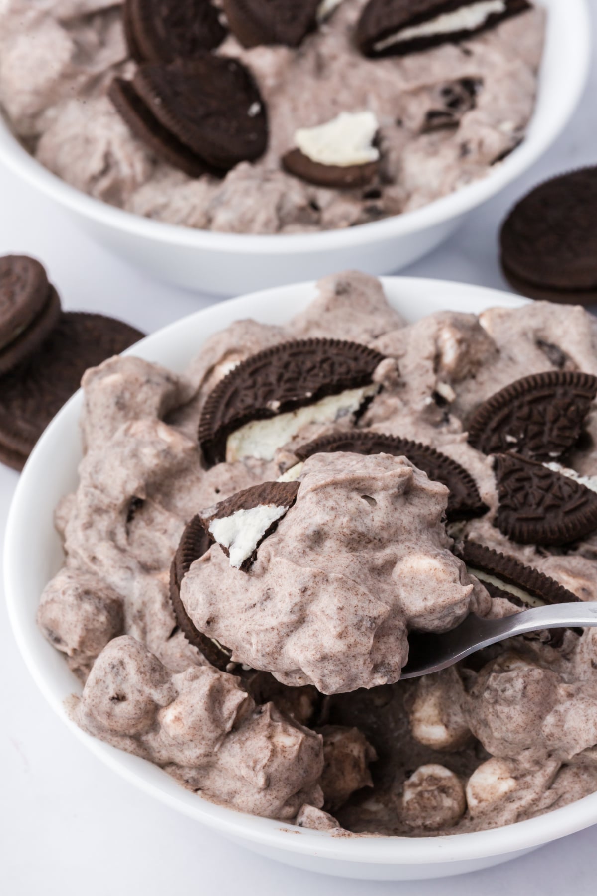 Fluff topped with crushed Oreo cookies and mini marshmallows in a bowl with a spoon.