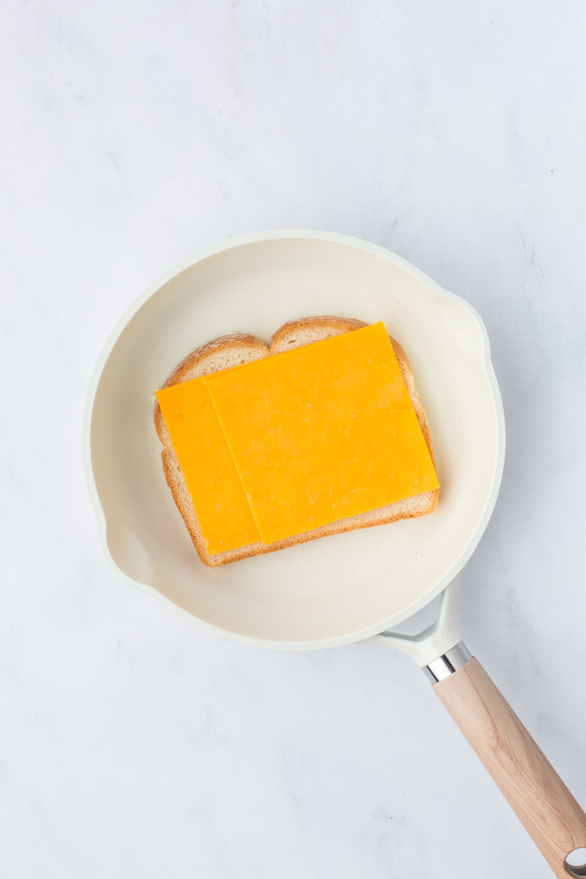 Bread buttered side down in skillet with cheddar cheese on top.