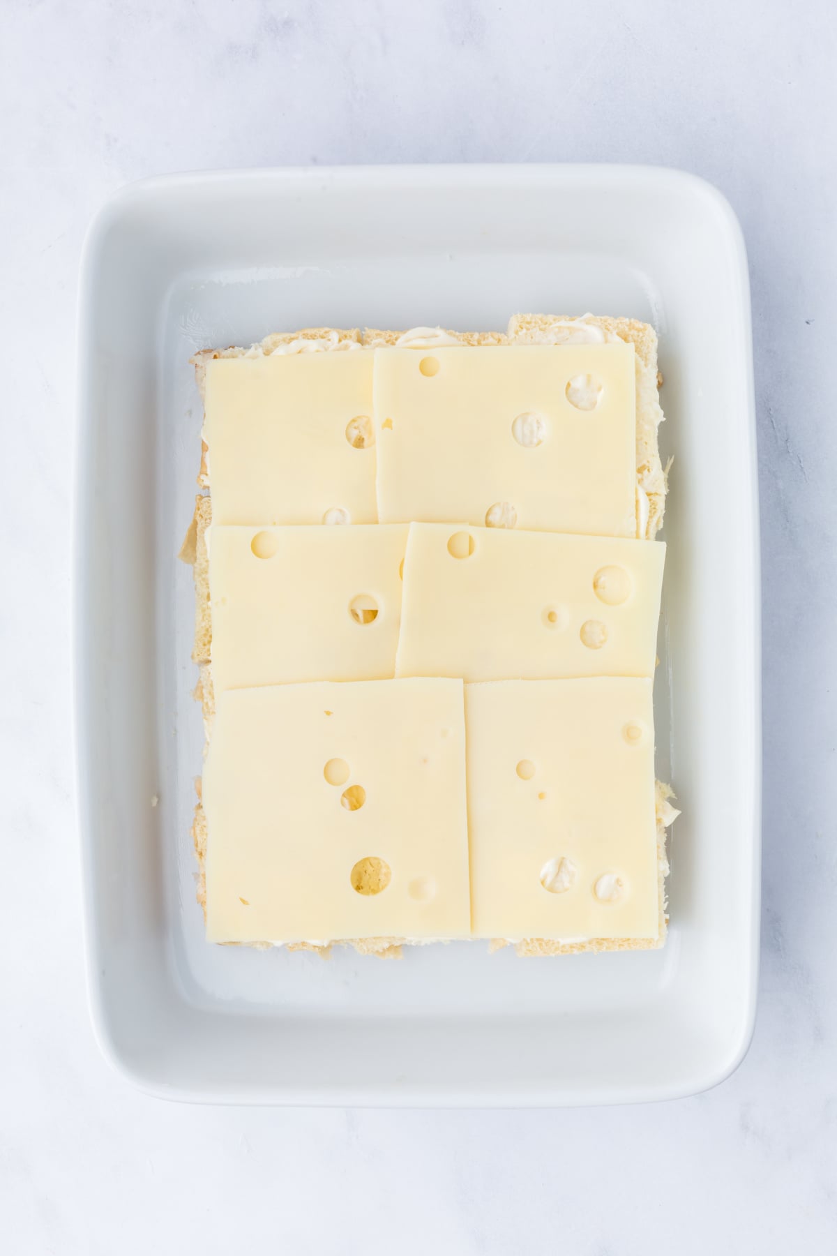 Bottom half of toasted Hawaiian rolls placed in a baking dish and spread with mayonnaise and Swiss cheese.