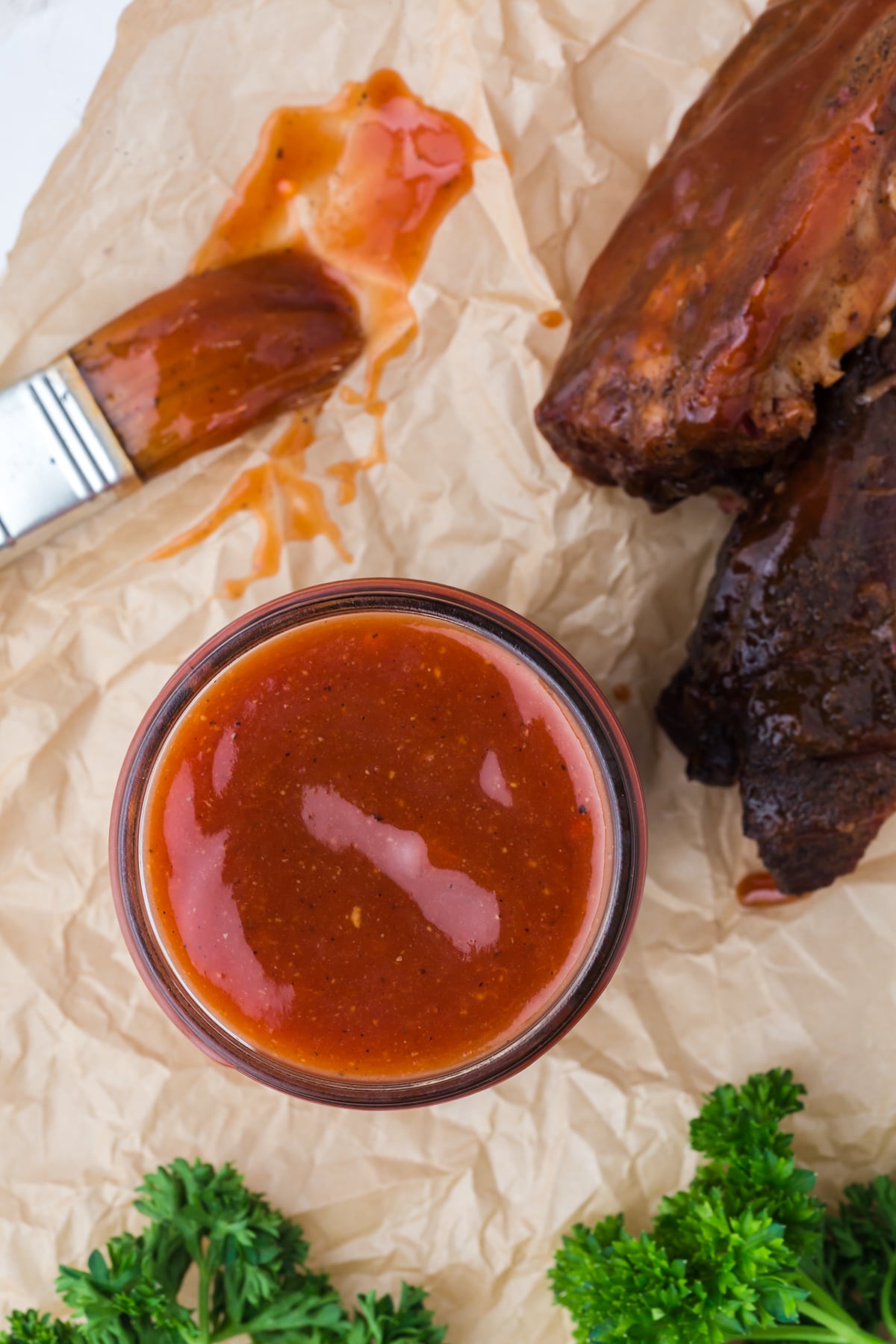 A jar of BBQ Sauce with a brush of bbq sauce and two pork ribs.