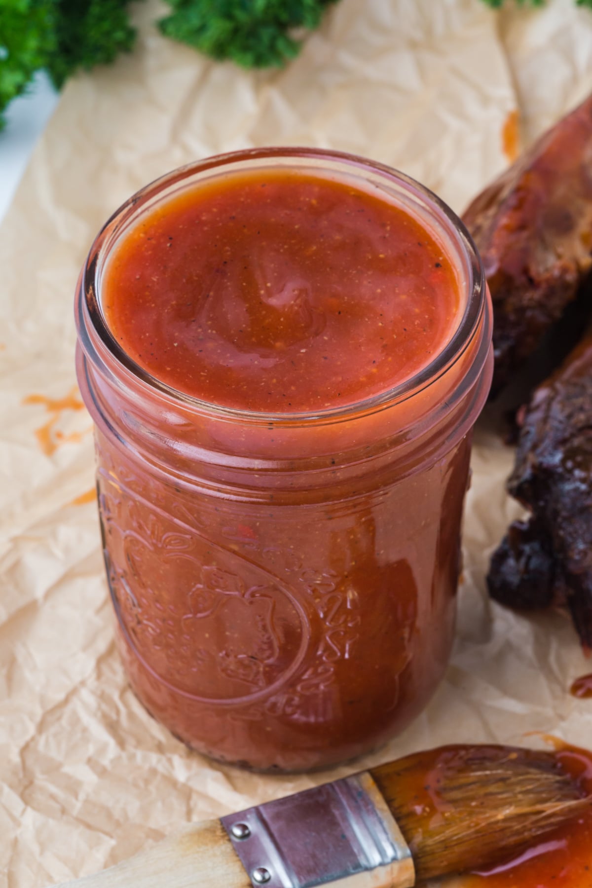 Jar filled with homemade hot honey BBQ sauce on a parchment-lined surface.