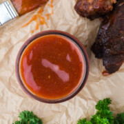 Jar of hot honey BBQ sauce with a basting brush and pork ribs on a parchment covered table.