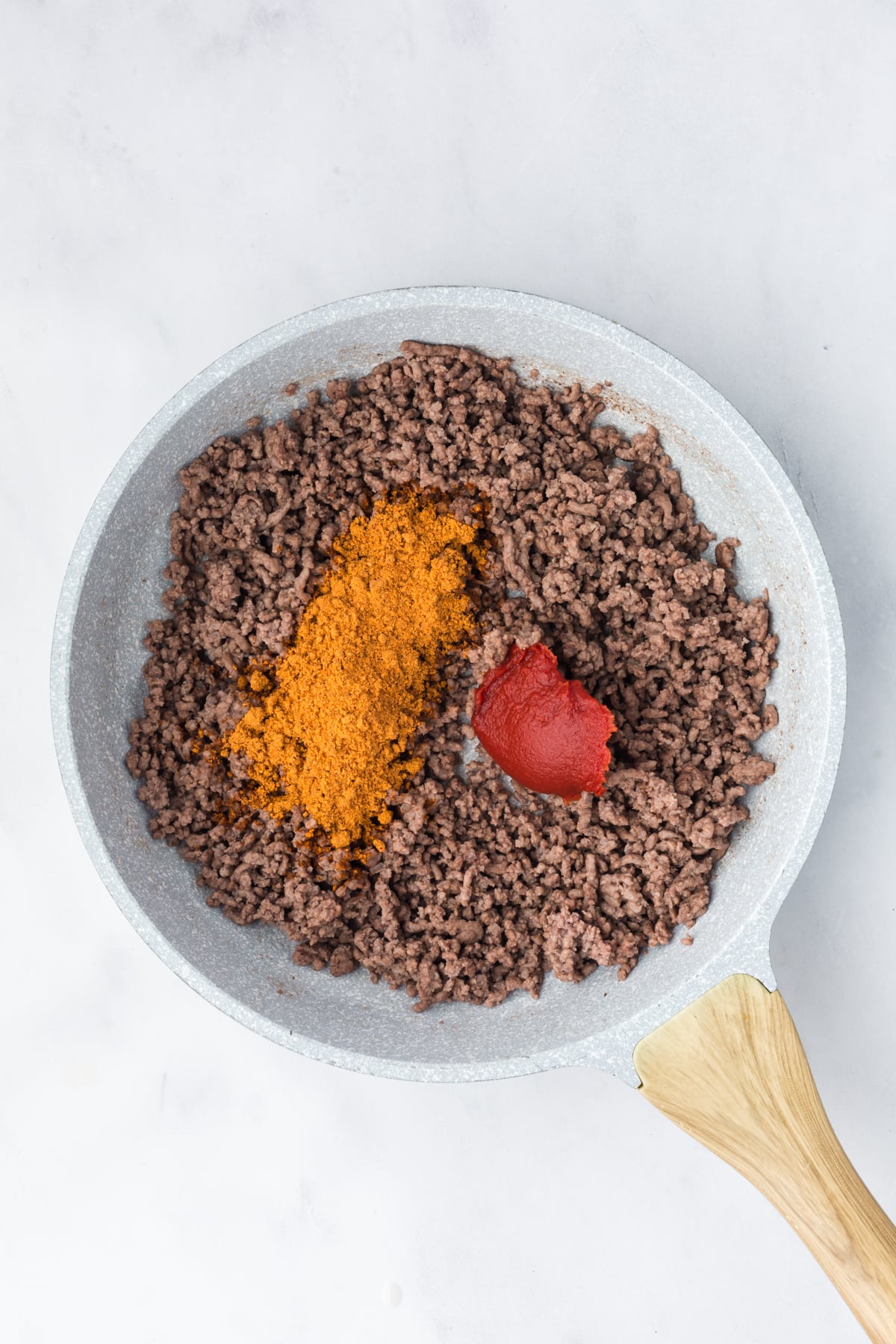 Cooked ground beef in a skillet with tomato paste and taco seasoning