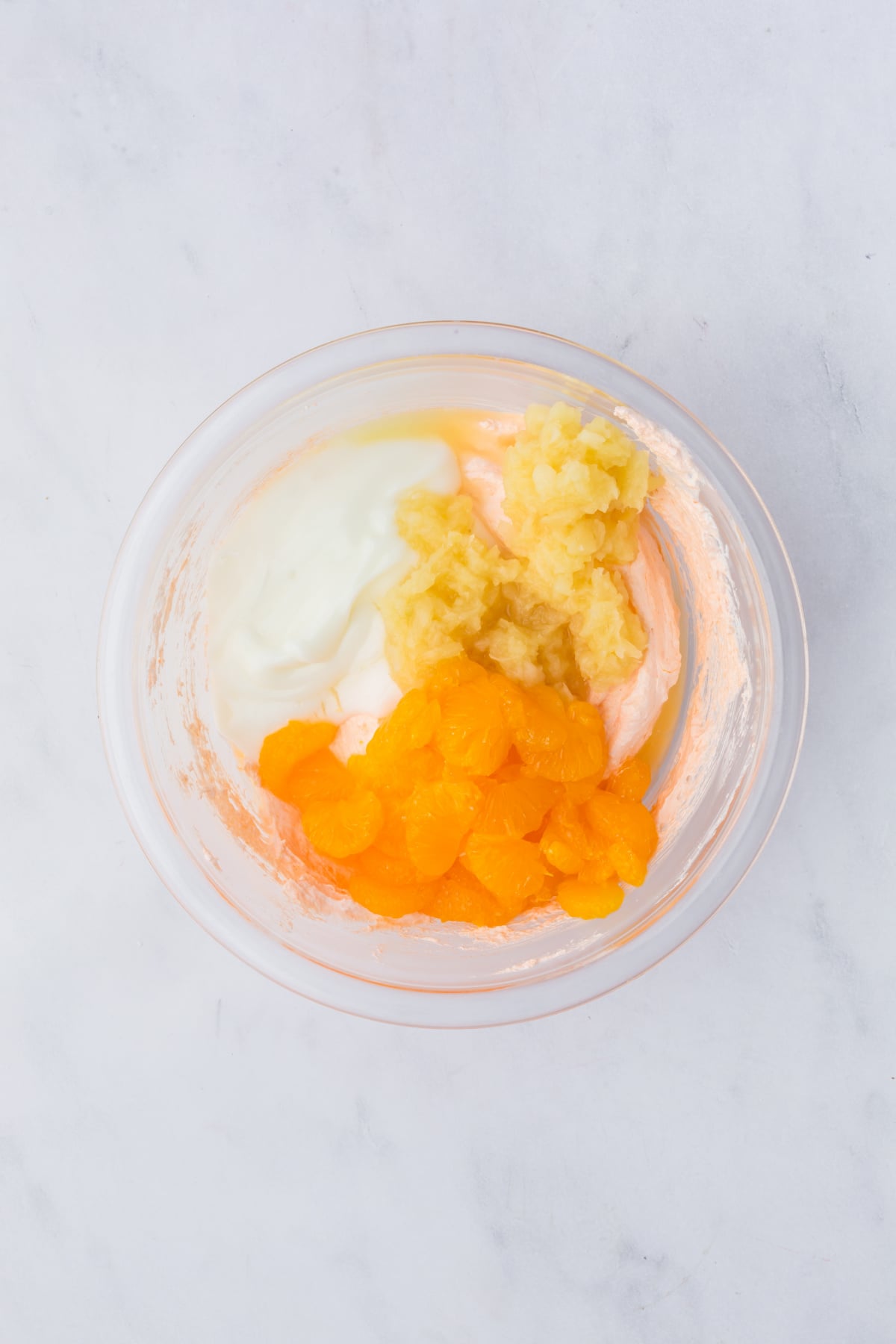 A large mixing bowl of fluff with crushed pineapple and mandarin oranges on top ready to be stirred.