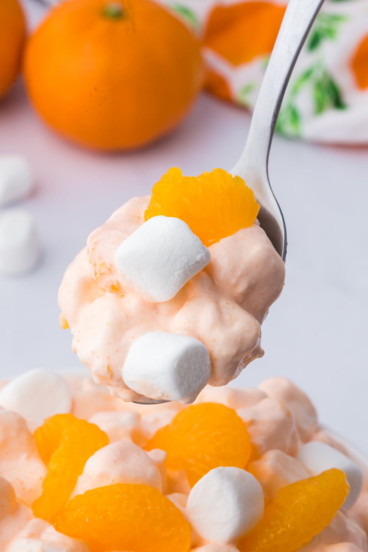 Spoonful of fluff with marshmallows and oranges above a serving bowl.