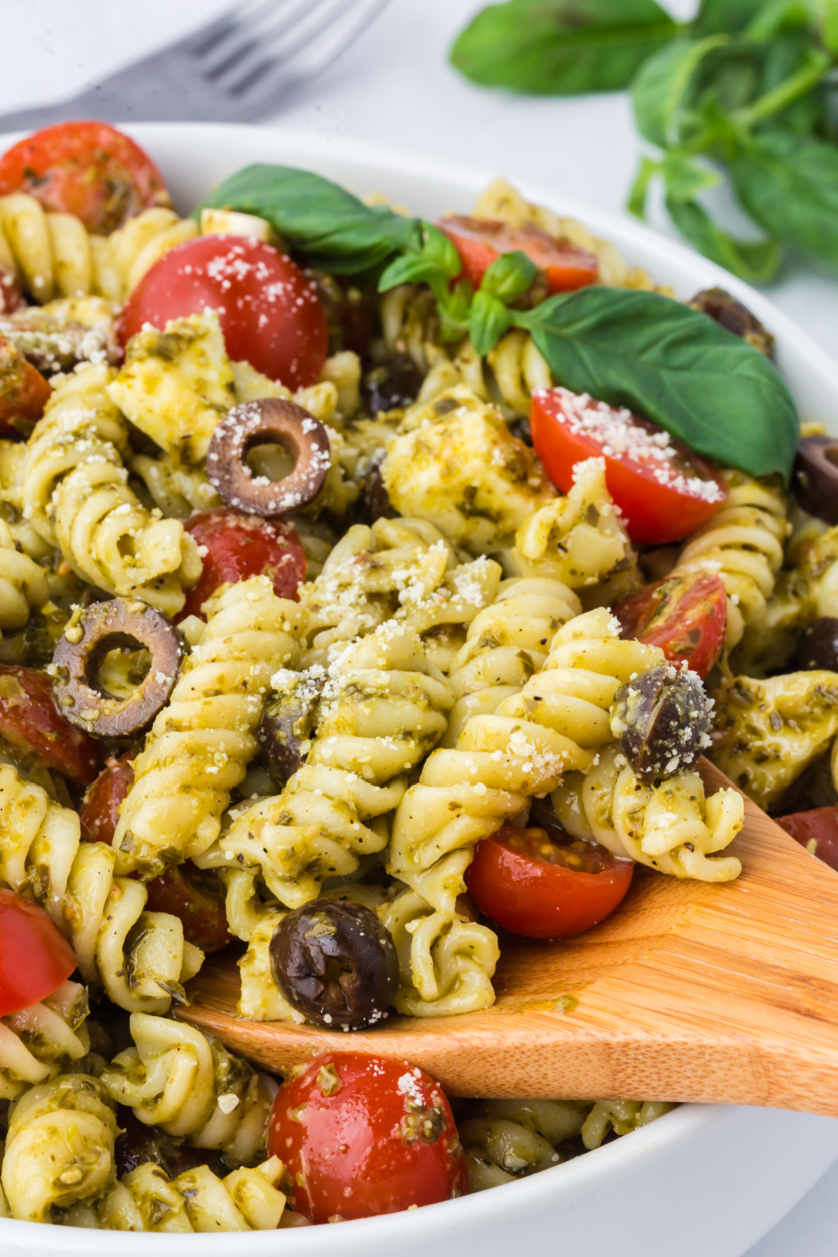 A wooden spoon removing a spoonful of pesto pasta salad vegetarian from a bowl.