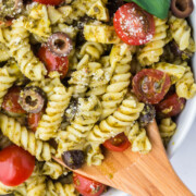 A wooden spoon removing a spoonful of Pesto Pasta Summer Salad from a bowl.