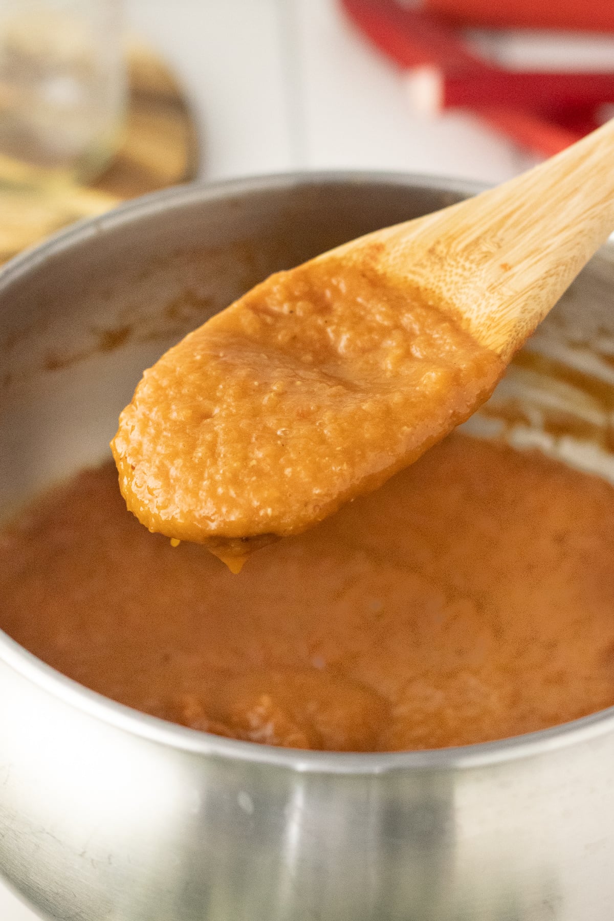 A wooden spoonful of smooth sauce lifted out of pot.