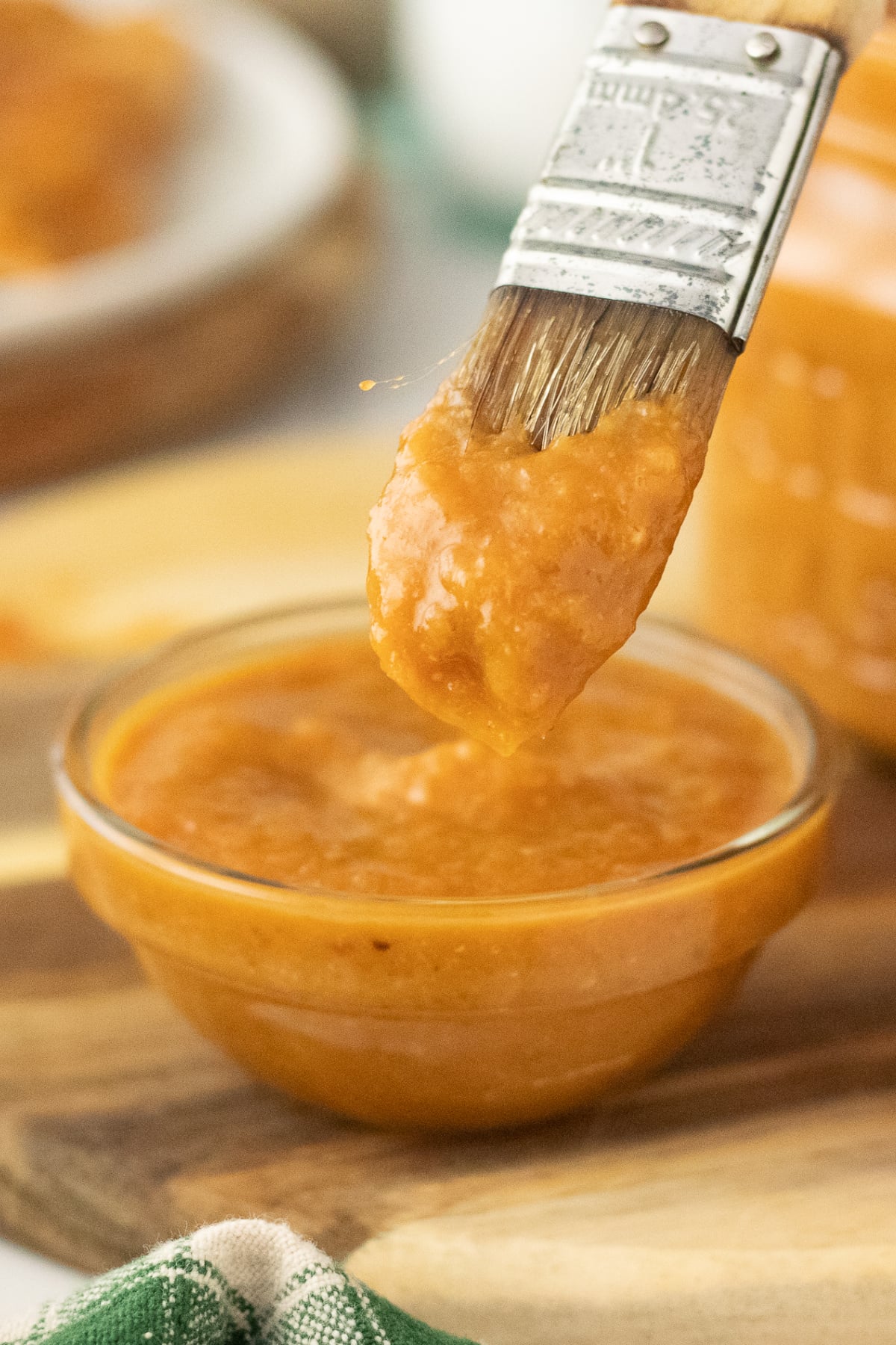 A brush full of dripping sauce lifted out of bowl of sauce. 