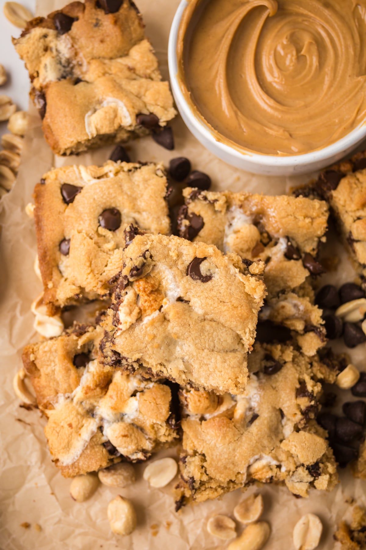 A pile of bars on parchment paper with a bowl of peanut butter.