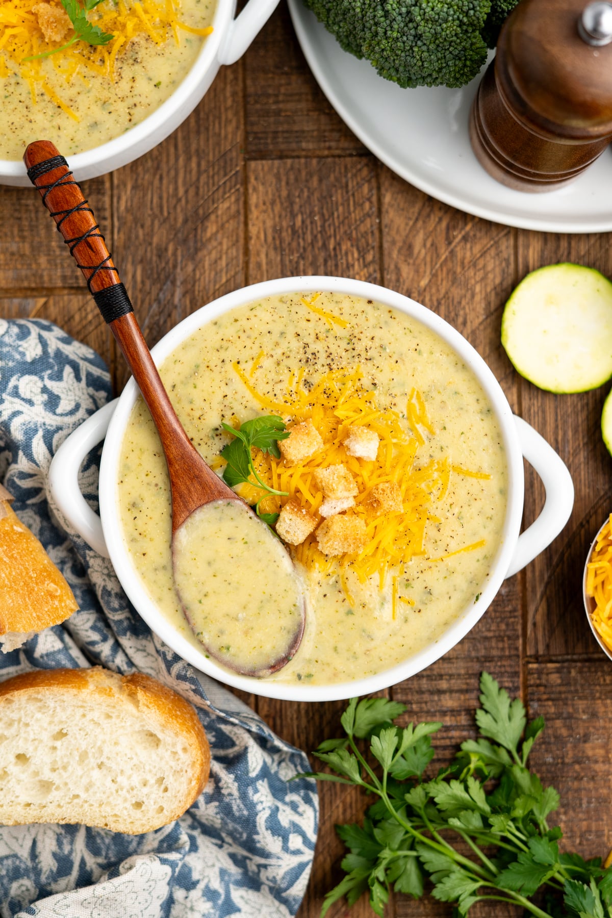 A bowl with potato zucchini soup and a wooden spoon on the side.