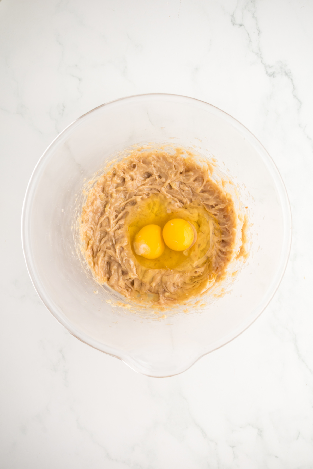 Mashed bananas, coconut oil, peanut butter blended in bowl with two eggs in bowl ready to be blended.