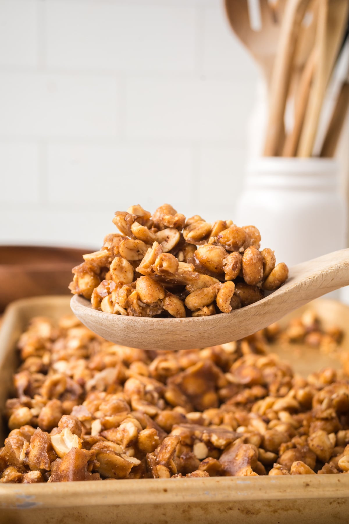 Wooden spoon filled with peanuts above a baking sheet.