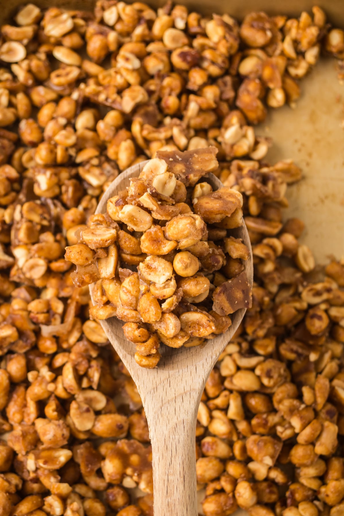 A wooden spoonful of baked peanuts held in the air above a panful