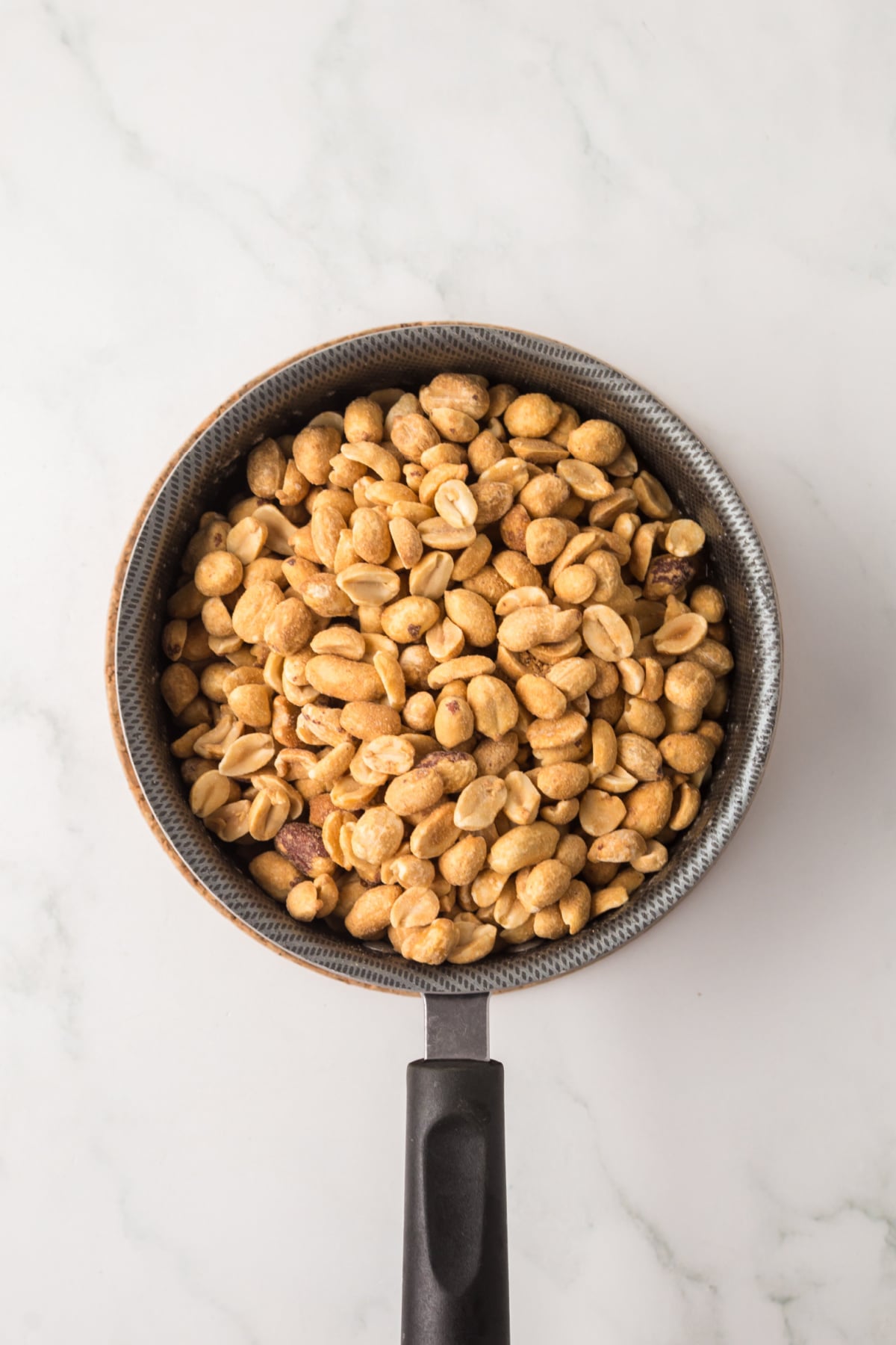 Roasted peanuts being stirred into warm butter toffee mixture in a saucepan.
