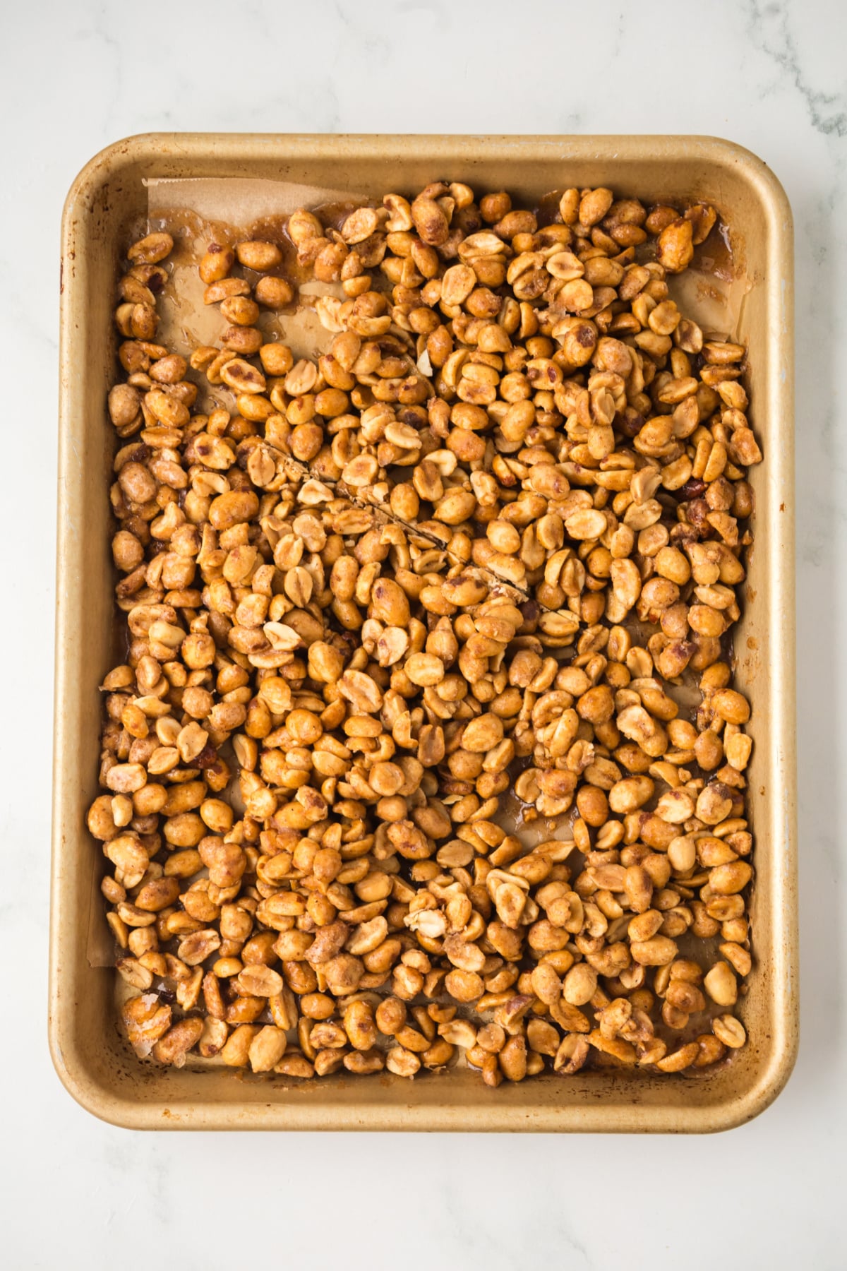Butter toffee coated peanuts spread on a parchment-lined baking sheet before baking.