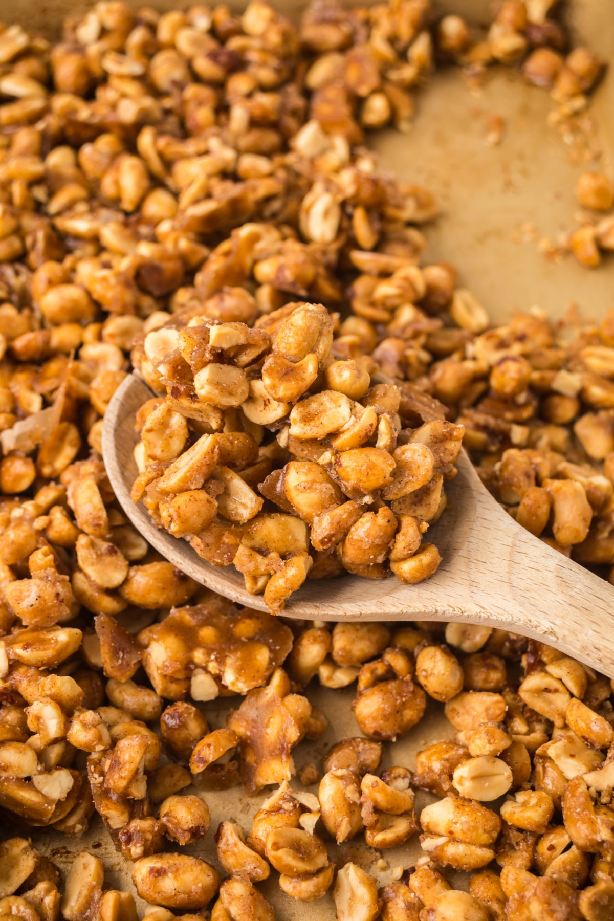 Freshly baked butter toffee peanuts cooling on a baking sheet while being stirred with a wooden spoon.