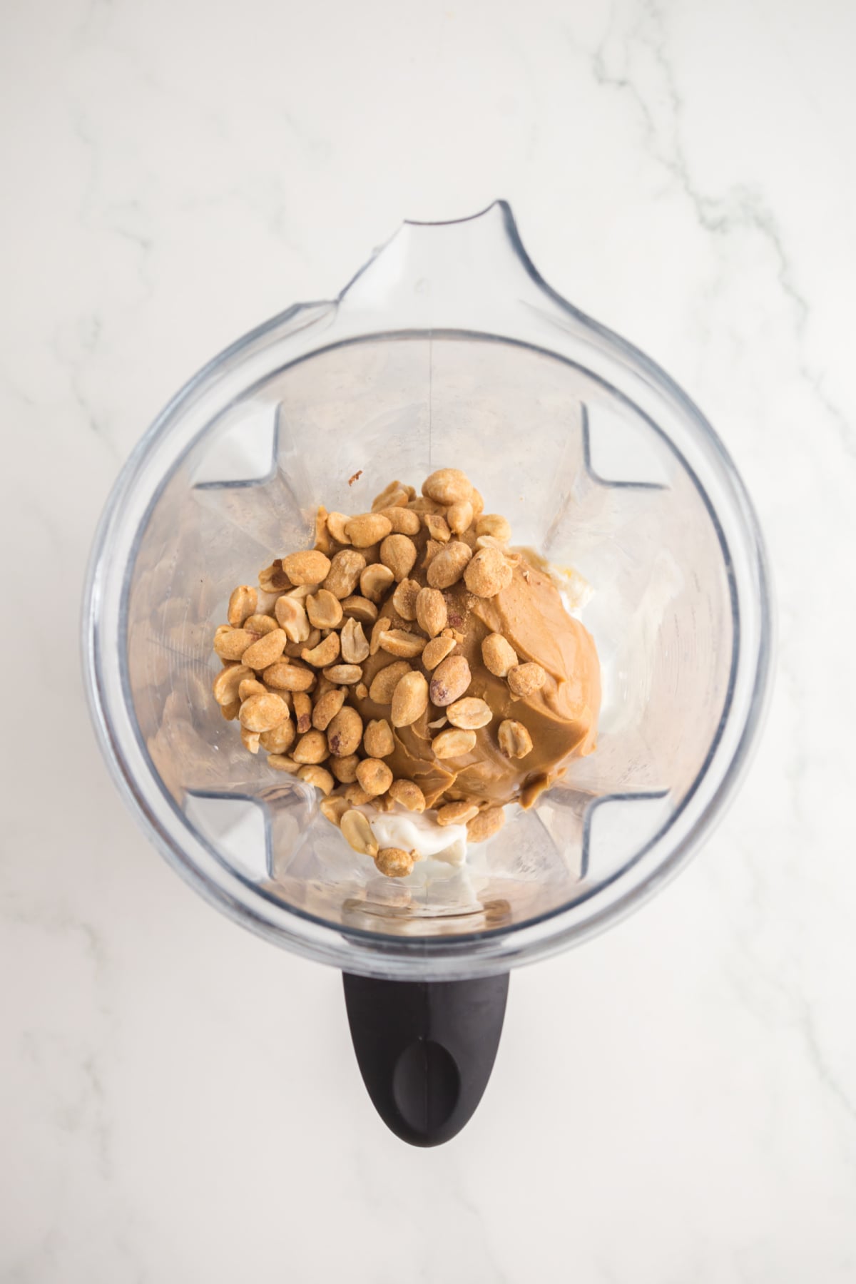 A blender with ice cream, peanut butter, peanuts, and milk in it.