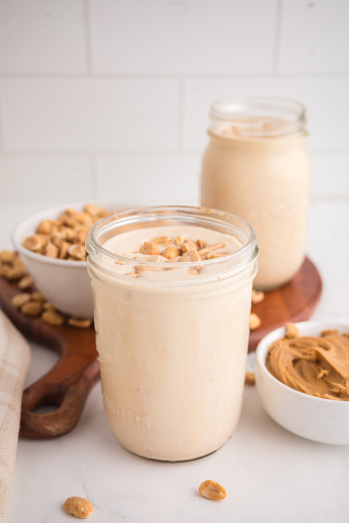 A milkshake with peanut butter in a jar with peanuts on top on a table.