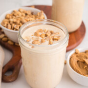 A peanut butter milkshake in a jar with a sprinkling of peanuts on top on a table.