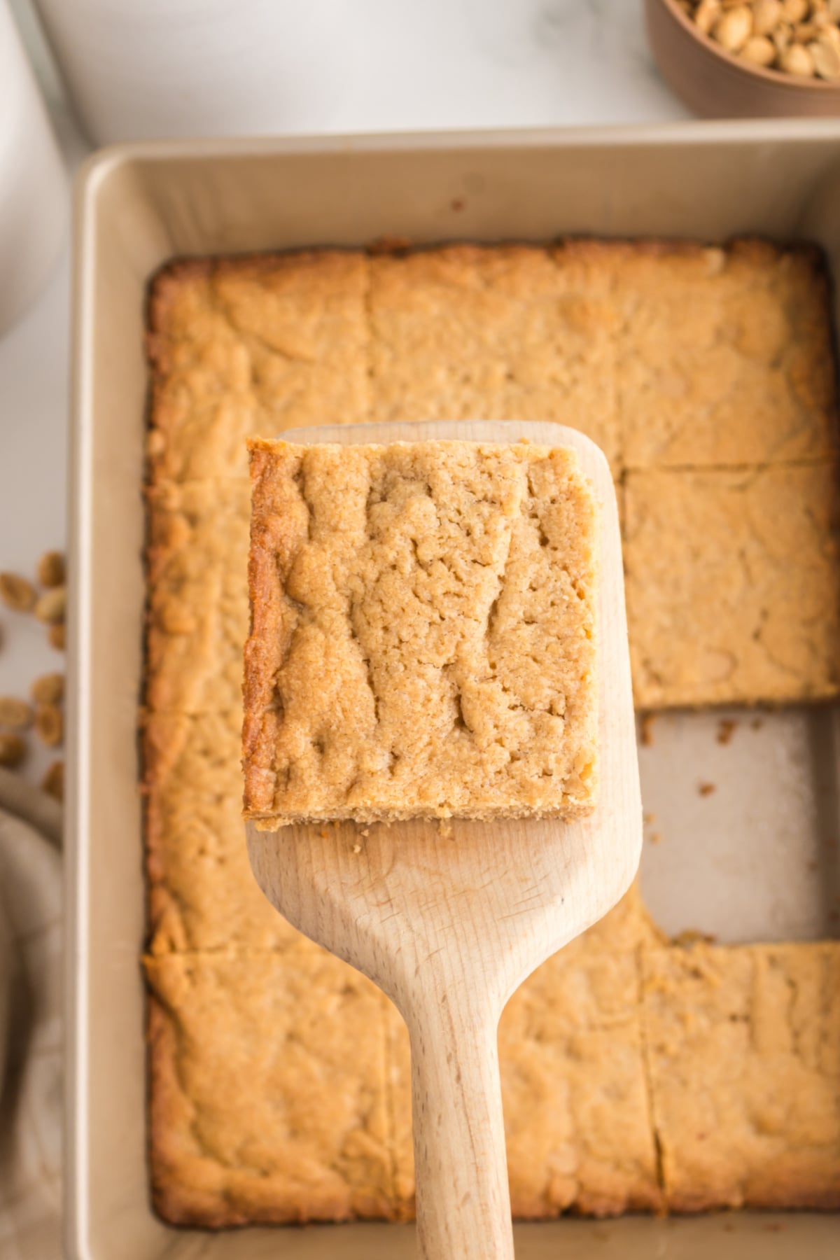 A blondie on a spatula held in the air above a panful.
